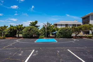 Ein Basketballplatz im Freien mit blauer Spielfläche, umgeben von Bäumen und Wohnhäusern.