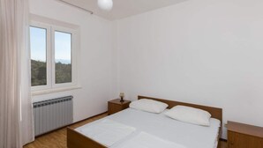 A bedroom with a bed, a nightstand, a window, and a radiator. - Rooms Villa Basica - Basic Double Room With Forest View (Mljet)