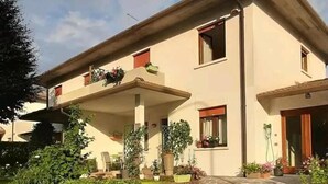 Un edificio de dos pisos con entrada empedrada en piedra, un porche cubierto con plantas en macetas y un muro de ladrillo.