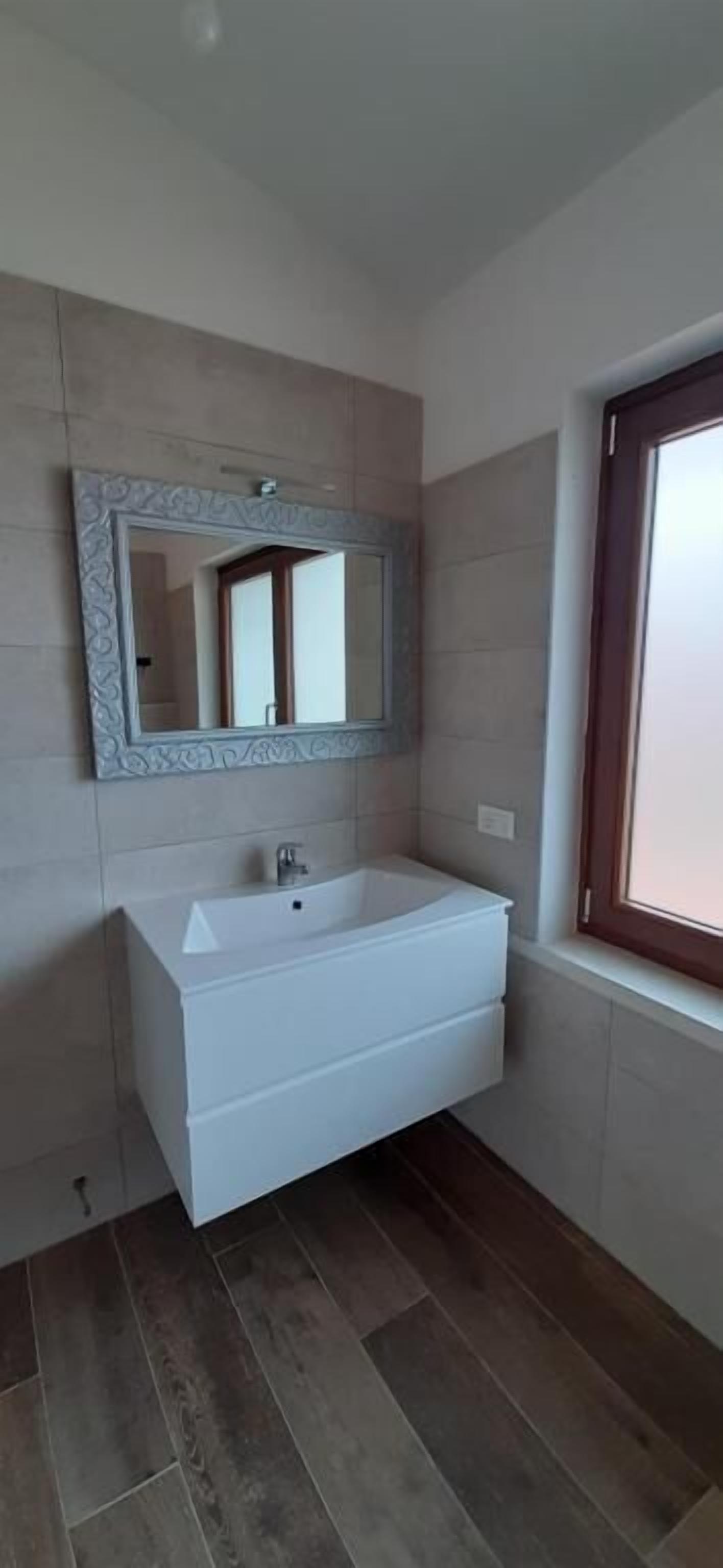 A bathroom with a white sink, a mirror with a decorative frame, and a window with a wooden frame.
