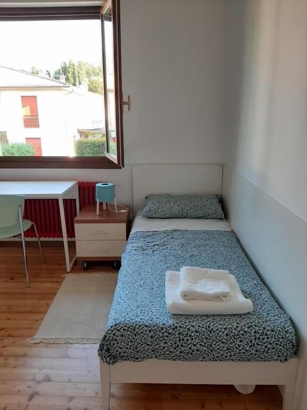 A small bedroom with a bed, a desk, and a window.