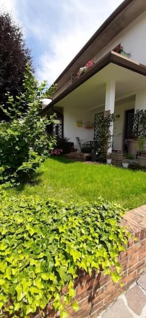 A house with a covered porch, a brick wall with ivy, and a grassy yard. - Alloggio il Giglio (Schio)