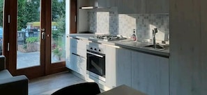 A modern kitchen with a gas stove, oven, and sink, and a sliding glass door leading to a patio area. - Alloggio il Giglio (Schio)