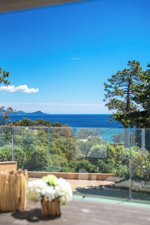 Ein Balkon mit Blick auf das Meer und ferne Berge, umgeben von viel Grün.