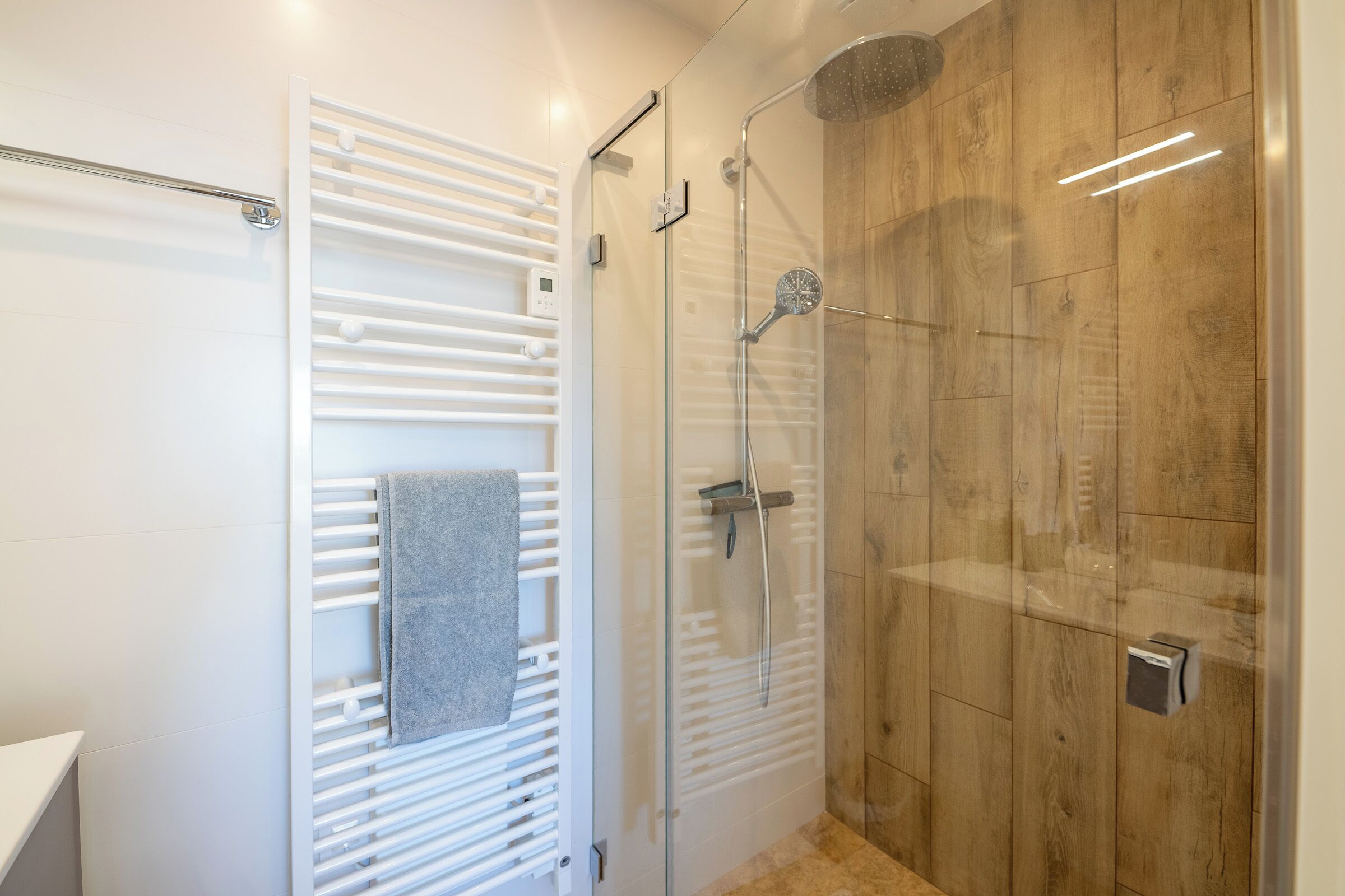A modern bathroom with a glass shower enclosure, a towel rack, and a wooden wall.