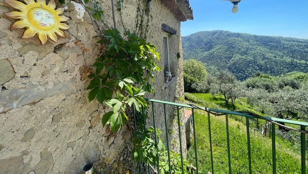 Un edificio rústico de piedra con un adorno de sol, una lámpara de metal y vistas a un valle verde.