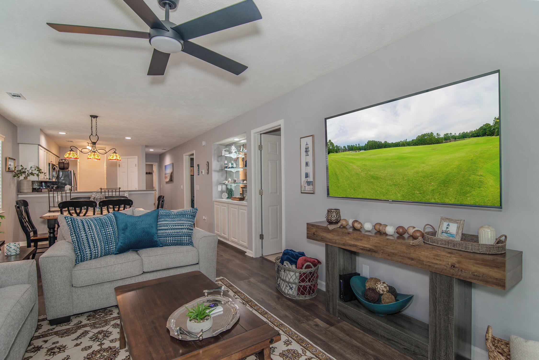 A living room with a ceiling fan, a large flat-screen TV, a fireplace, and a dining area with chairs and a table.