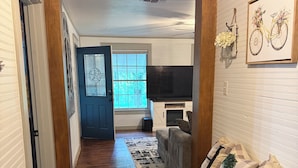 A hallway leading to a living room with a fireplace, a sofa with patterned cushions, and a wall-mounted bicycle artwork. - Wonderful 3-bedroom cottage in charming Diboll (Diboll)
