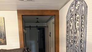 A hallway with a wooden floor, a gray sofa with patterned pillows, a black and white rug, and a decorative metal wall piece. - Wonderful 3-bedroom cottage in charming Diboll (Diboll)