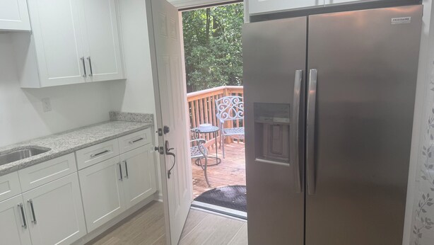 A kitchen with white cabinets, a stainless steel refrigerator, and a wooden deck with outdoor seating. - Cozy 1-BR/BA cottage in beautiful Stonecrest near I-20 & I-285, Arabia Mountain (Stonecrest)