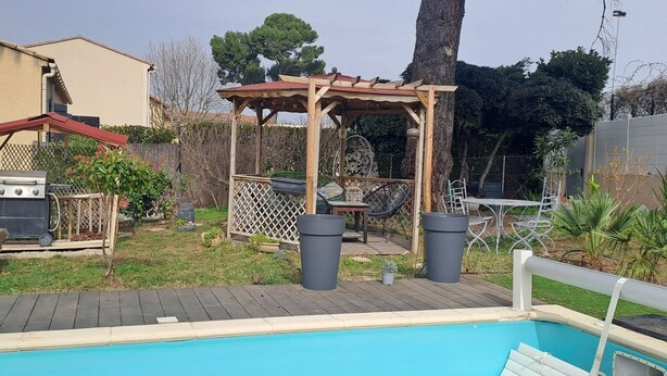 Un giardino sul retro con piscina, barbecue, un pergolato in legno e un'area giardino recintata.