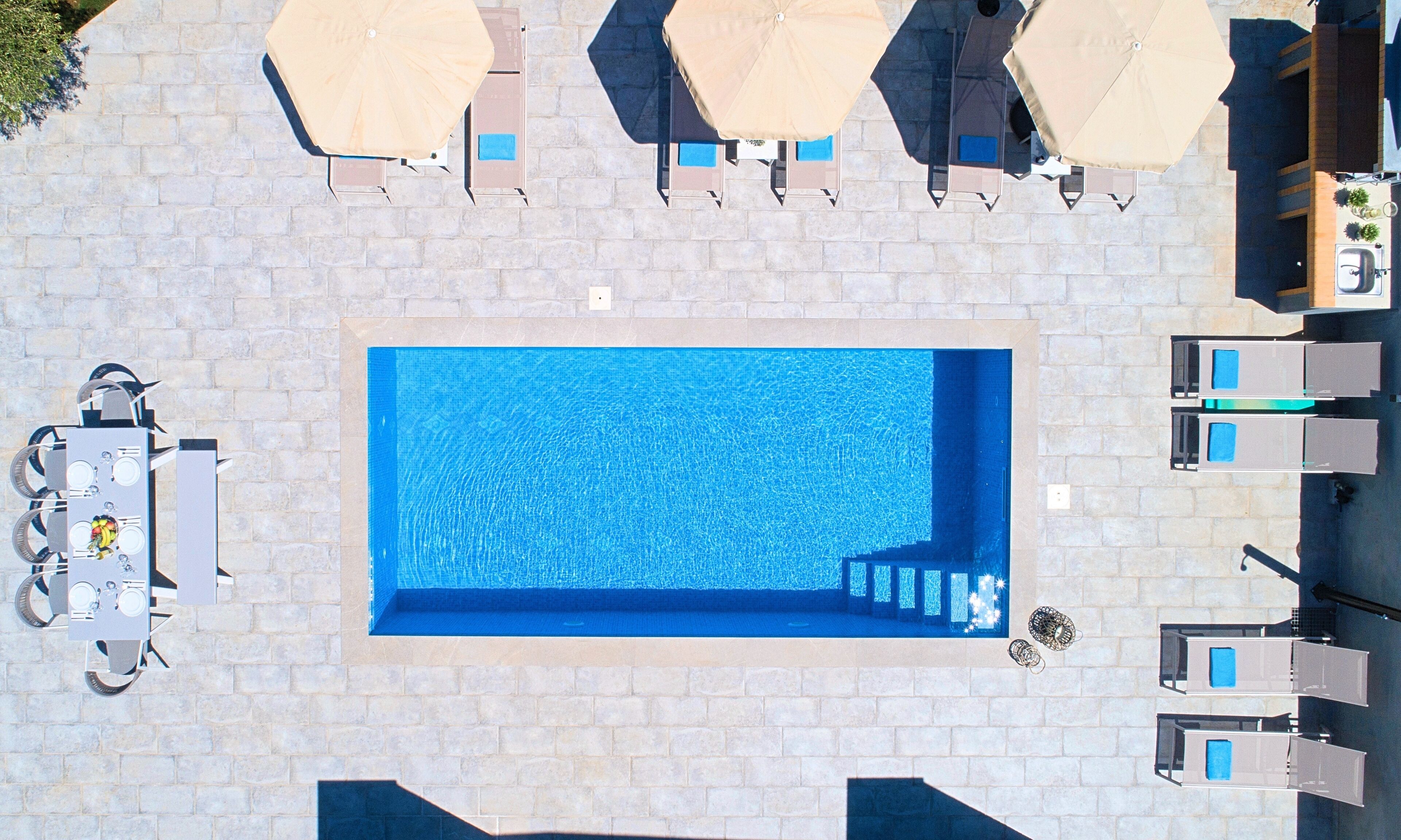 Ein Pool auf dem Dach mit glatter, blauer Wasseroberfläche, umgeben von Liegestühlen und Sonnenschirmen.