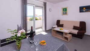 A modern living room with a sofa, a dining table with a vase of flowers, a wine bottle, and glasses. - Peaceful Apartments Harfa- One Bedroom Apartment With Balcony and Partial Sea View 2 (Orebic)