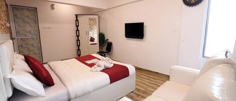A hotel room with a bed, a white sofa, a TV, a clock, and a window.