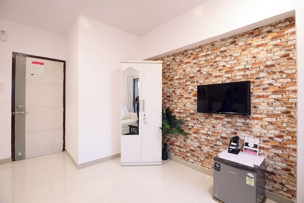 Un área de recepción con pared de ladrillo, televisor de pantalla plana, perchero, máquina expendedora y armario blanco.