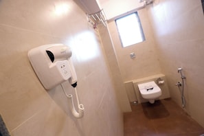 Un baño con un secador de pelo fijado a la pared, un inodoro con cara de caricatura y una ventana pequeña.