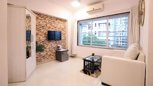 Una sala de estar con pared de ladrillo, un televisor de pantalla plana, un sofá, una mesa de centro y una ventana con vistas a edificios.