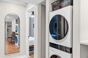 A laundry room with a washing machine, a dryer, and a mirror reflecting a bedroom with a bed and a chair. - Remodeled, Steps from Main Street Shops, Dining & Slopes (Breckenridge)