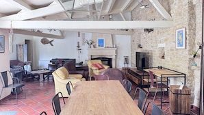 A spacious living area with a wooden dining table, comfortable seating, a fireplace, and a stone wall. - Charming house near Chaucre Beach (Saint-Georges-d'Oléron)