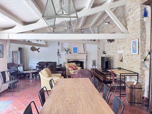 Uma sala de estar ampla com mesa de jantar de madeira, assentos confortáveis, lareira e parede de pedra.