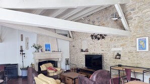 A living room with a fireplace, leather sofas, a TV, and stone walls. - Charming house near Chaucre Beach (Saint-Georges-d'Oléron)