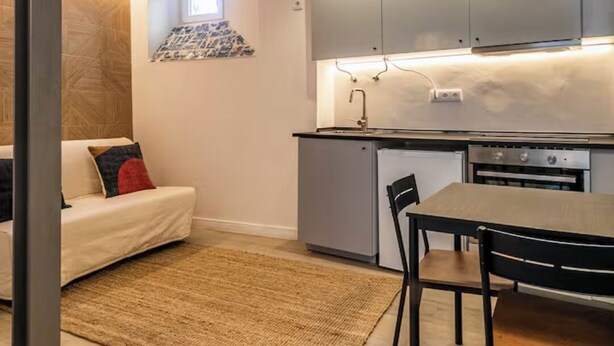 Une cuisine compacte dotée d’appareils électroménagers modernes, un coin repas avec une table et des chaises, et un espace salon confortable avec un canapé.