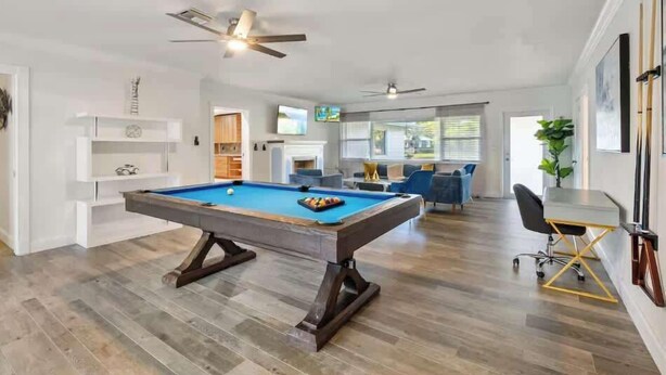 Une table de billard dans une pièce dotée d’un ventilateur de plafond, d’un coin cuisine et d’un espace salon avec un téléviseur.