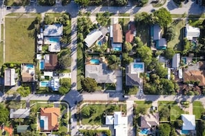 Eine Vogelperspektive eines Wohngebiets mit mehreren Häusern, von denen einige Swimmingpools haben, umgeben von Grünflächen und Straßen.