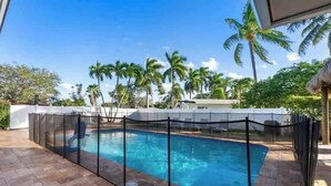 Une piscine entourée d’une clôture, avec des palmiers et un ciel dégagé.