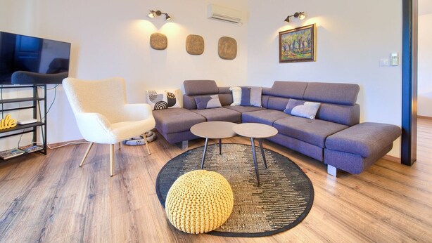 Ein modernes Wohnzimmer mit einem Ecksofa, einem weißen Sessel, einem runden Couchtisch, einem Fernseher und Wanddekoration.