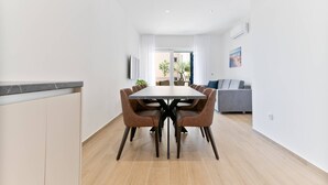 A modern dining area with a rectangular table, six chairs, and a grey sofa in the background. - Luxury Living at Horizon Retreat - Premium Two Bedroom Apartment (Marina)