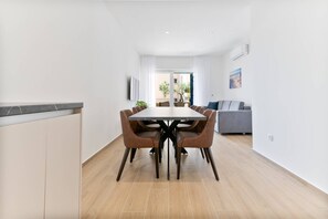Ein moderner Essbereich mit einem rechteckigen Tisch, sechs Stühlen und einem grauen Sofa im Hintergrund.