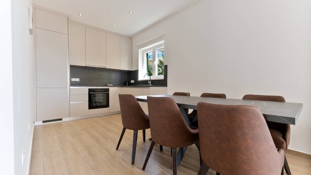 A modern kitchen with a dining area, featuring a large table and chairs, a window with a view, and recessed ceiling lights. - Luxury Living at Horizon Retreat - Premium Two Bedroom Apartment (Marina)