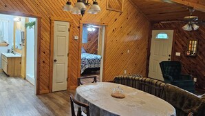 Puinen sisustus, jossa on ruokapöytä, tuoleja, sänky ja pieni keittiö.