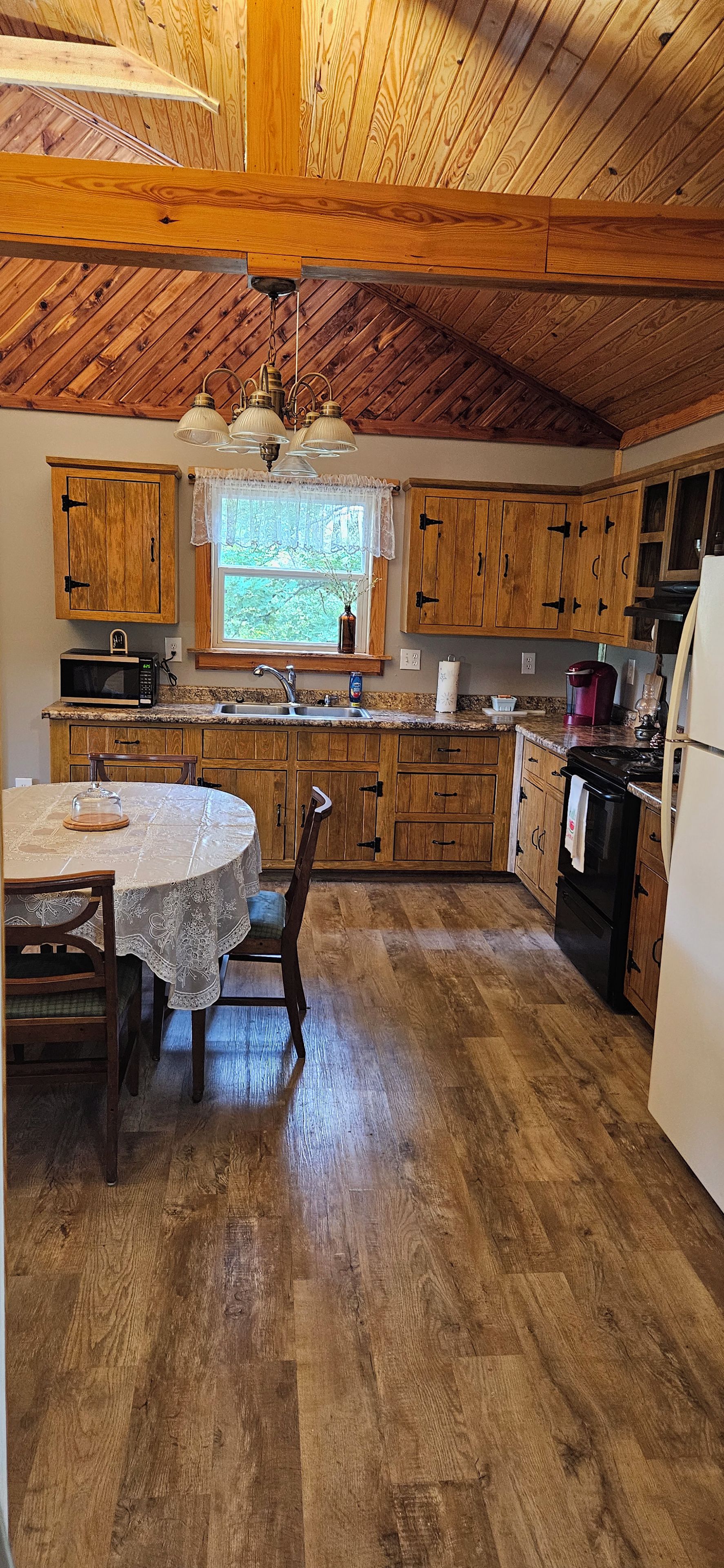 A kitchen with wooden cabinets, a dining table with chairs, a window with a view, and a ceiling with wooden beams.