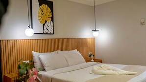 Un letto rifatto con lenzuola bianche, una testiera in legno, un comodino con un vaso di fiori e un'opera d'arte appesa al muro.