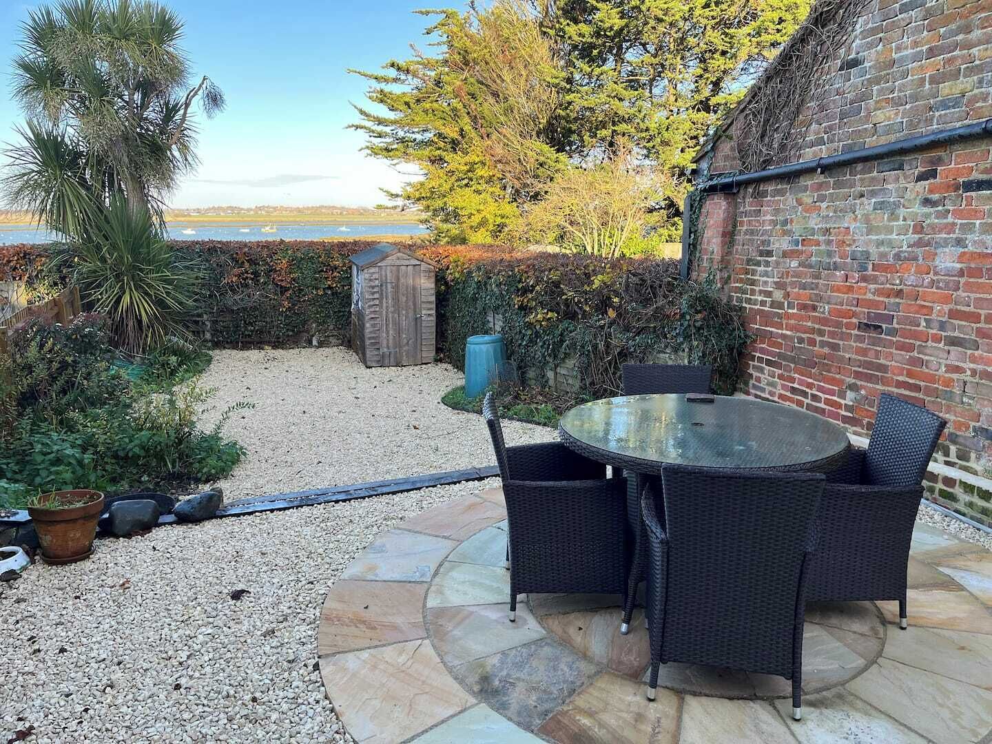 A patio with a round table and chairs, a small shed, and a brick wall.