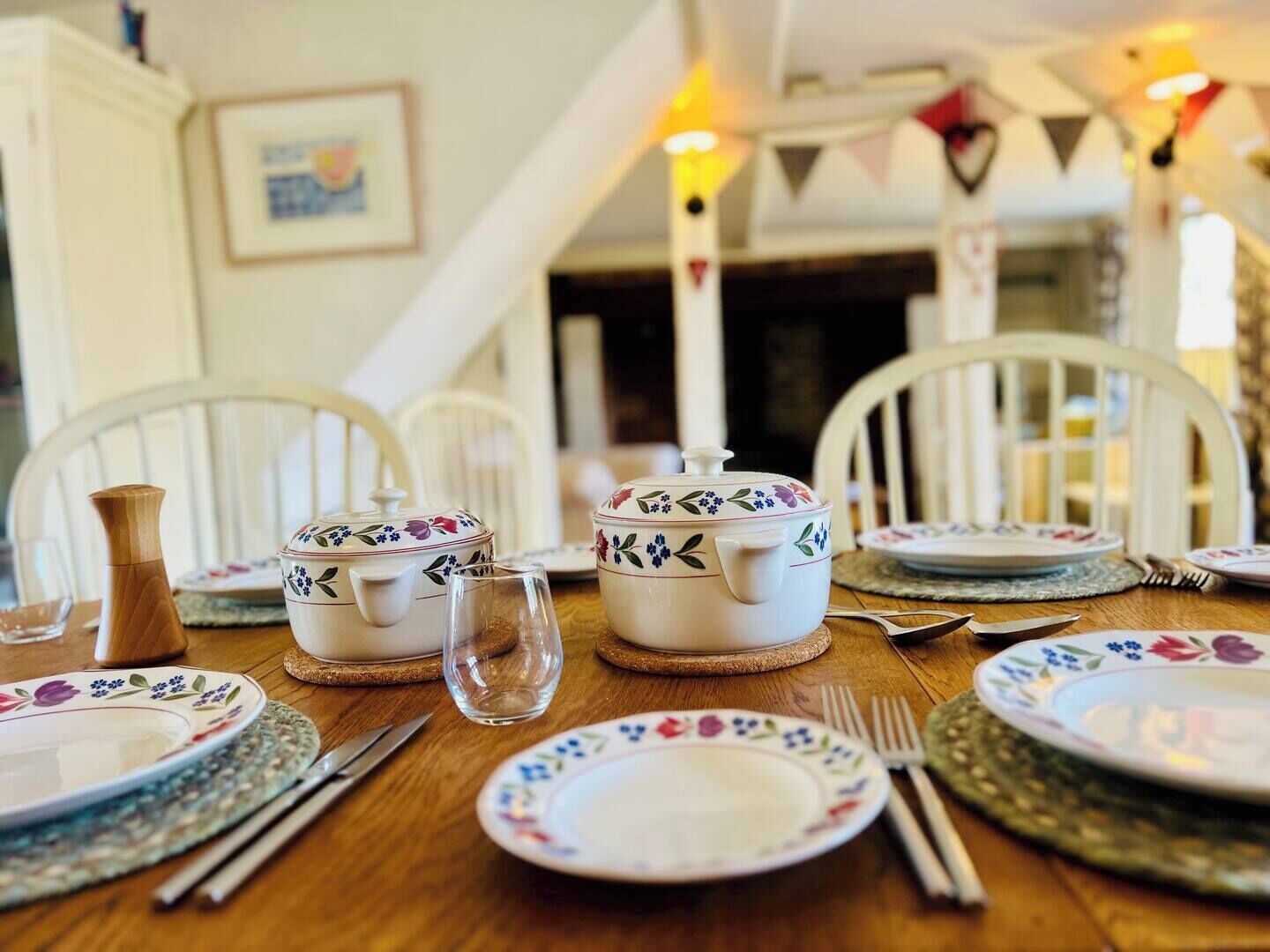 A dining table set with white chairs, floral-patterned plates, and a wooden pitcher.