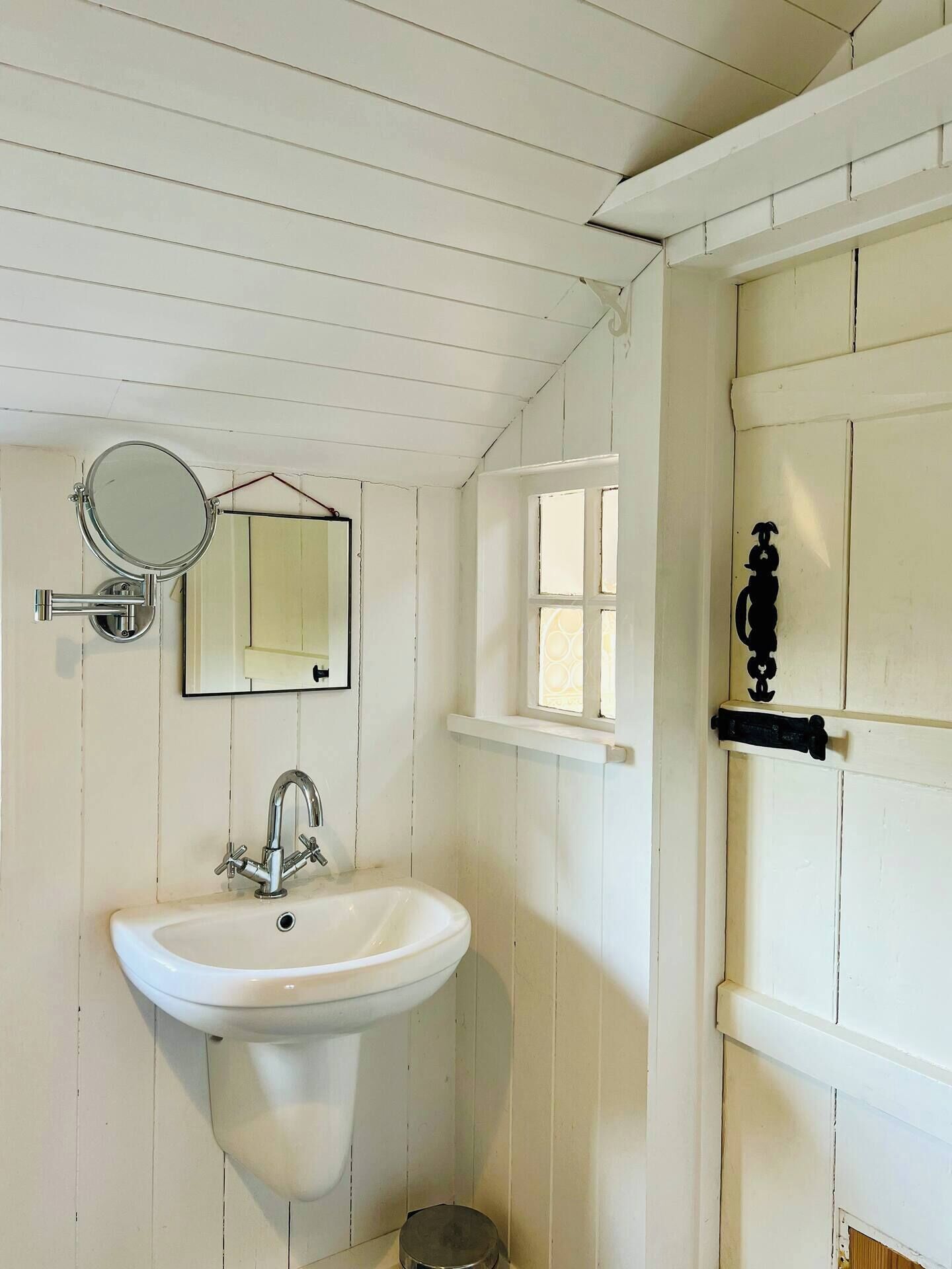 Een badkamer met een wit wastafel, spiegel en raam.