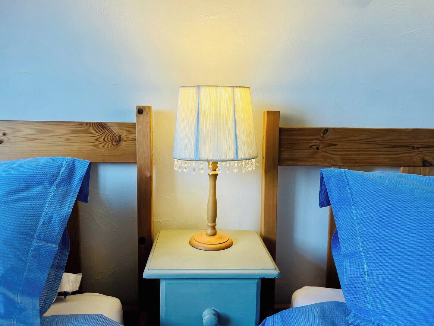 A small, simple room with a single bedside table, a lamp, and two beds.