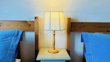 A small, simple room with a single bedside table, a lamp, and two beds.