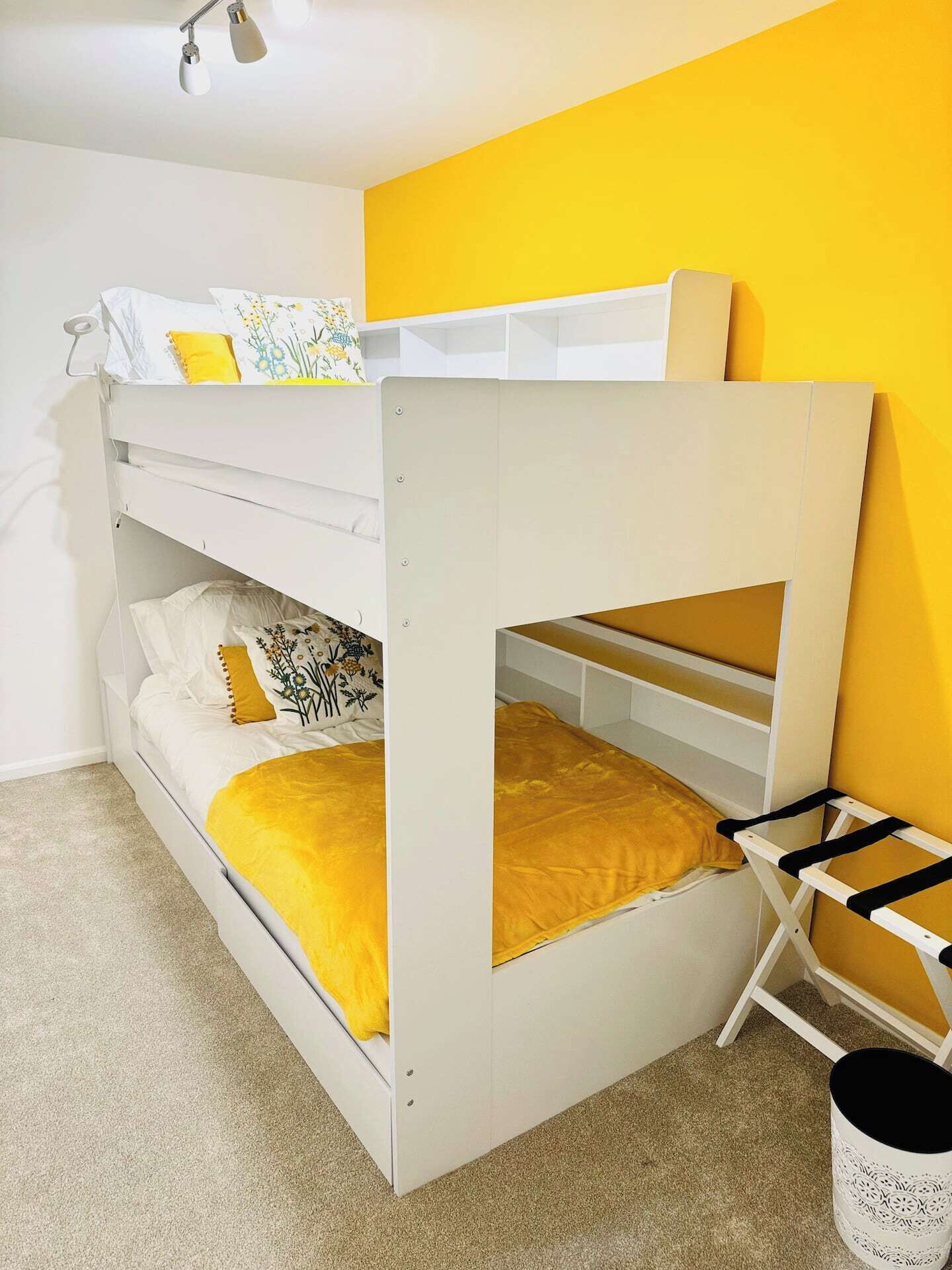 Ein Stockbett mit Schreibtisch und Leiter, ein kleiner Mülleimer und eine gelbe Wand.