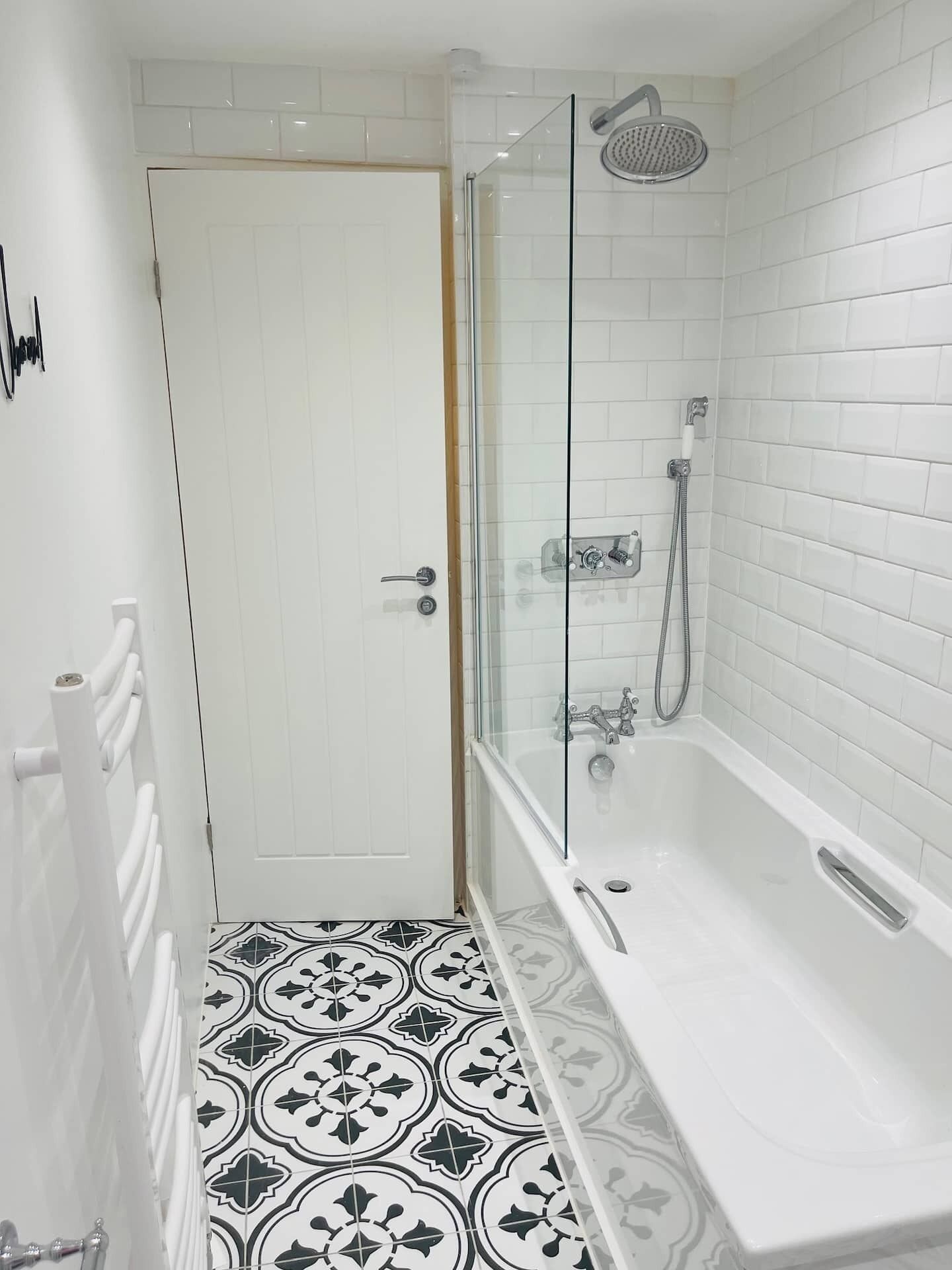 Une salle de bain dotée d’une douche à parois de verre, d’une baignoire blanche et de carreaux de sol à motifs.