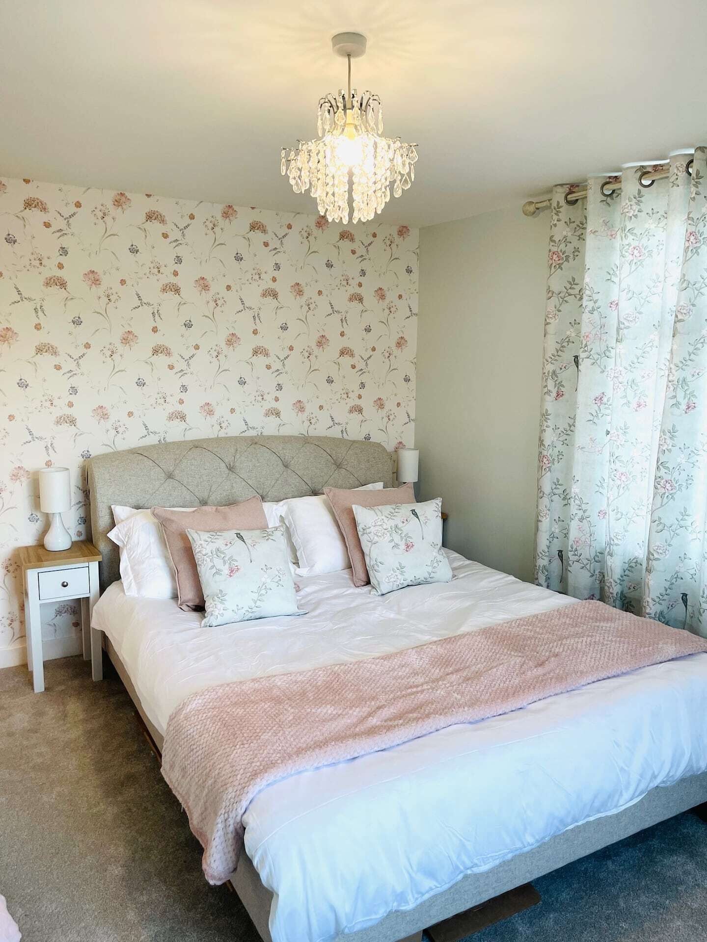Une chambre à coucher avec un lit, une table de chevet, une lampe, un papier peint à motifs floraux et un lustre.