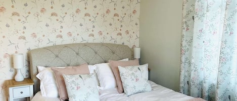 A bedroom with a bed, nightstand, lamp, floral wallpaper, and a chandelier.