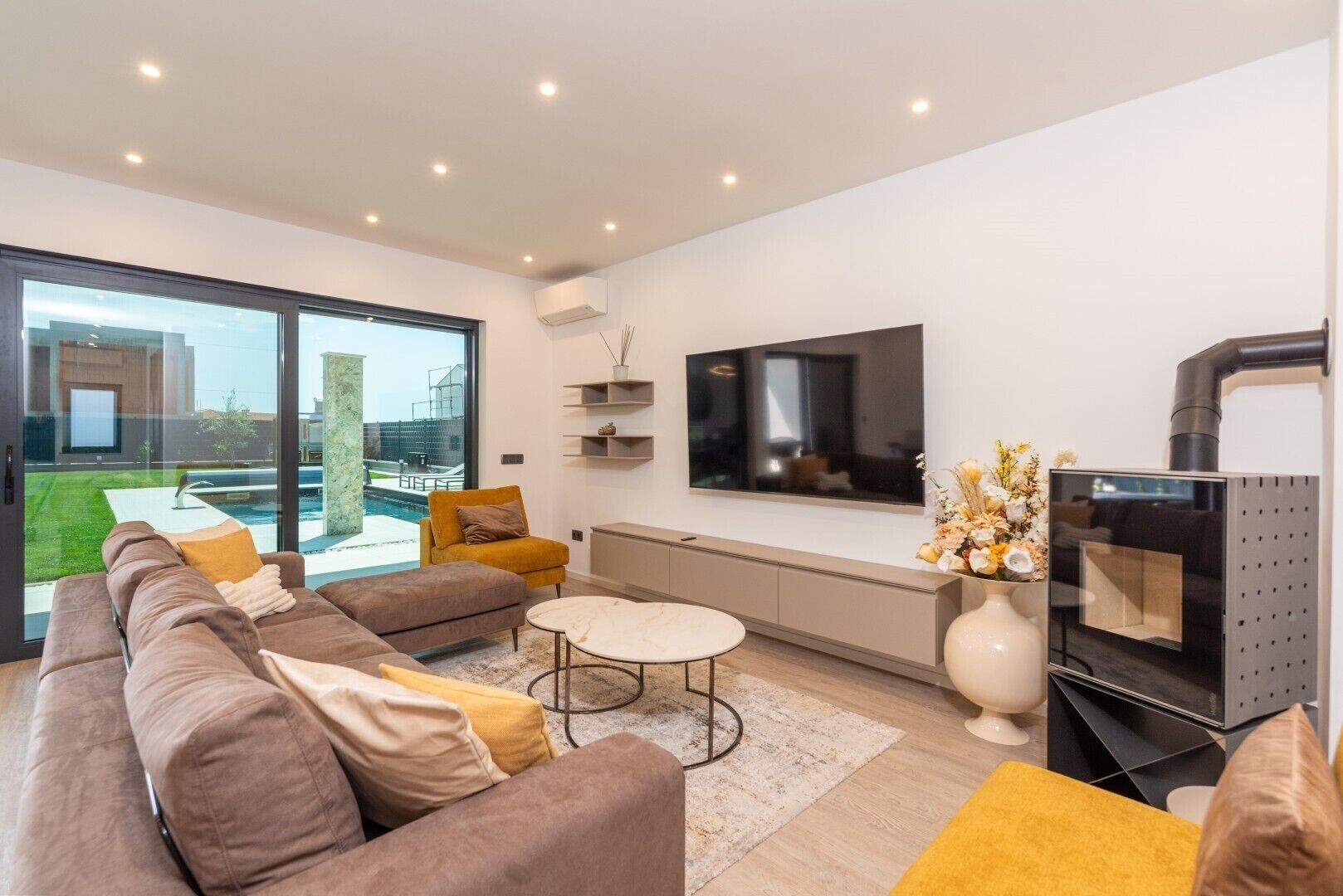 A modern living room with a large TV, comfortable seating, a fireplace, and a view of the outdoors.