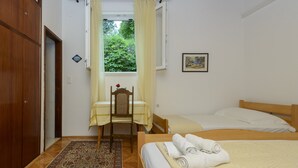 Ein Schlafzimmer mit Bett, Sessel, Tisch, Fenster mit Vorhängen und einer Tür.