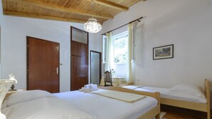 Ein Zimmer mit zwei Betten, einer Holzbalkendecke, einer Kristallleuchtre und einem Fenster mit Vorhängen. An der Wand hängt ein gerahmtes Bild.
