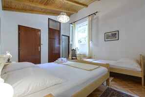 Ein Zimmer mit zwei Betten, einer Holzbalkendecke, einer Kristallleuchtre und einem Fenster mit Vorhängen. An der Wand hängt ein gerahmtes Bild.
