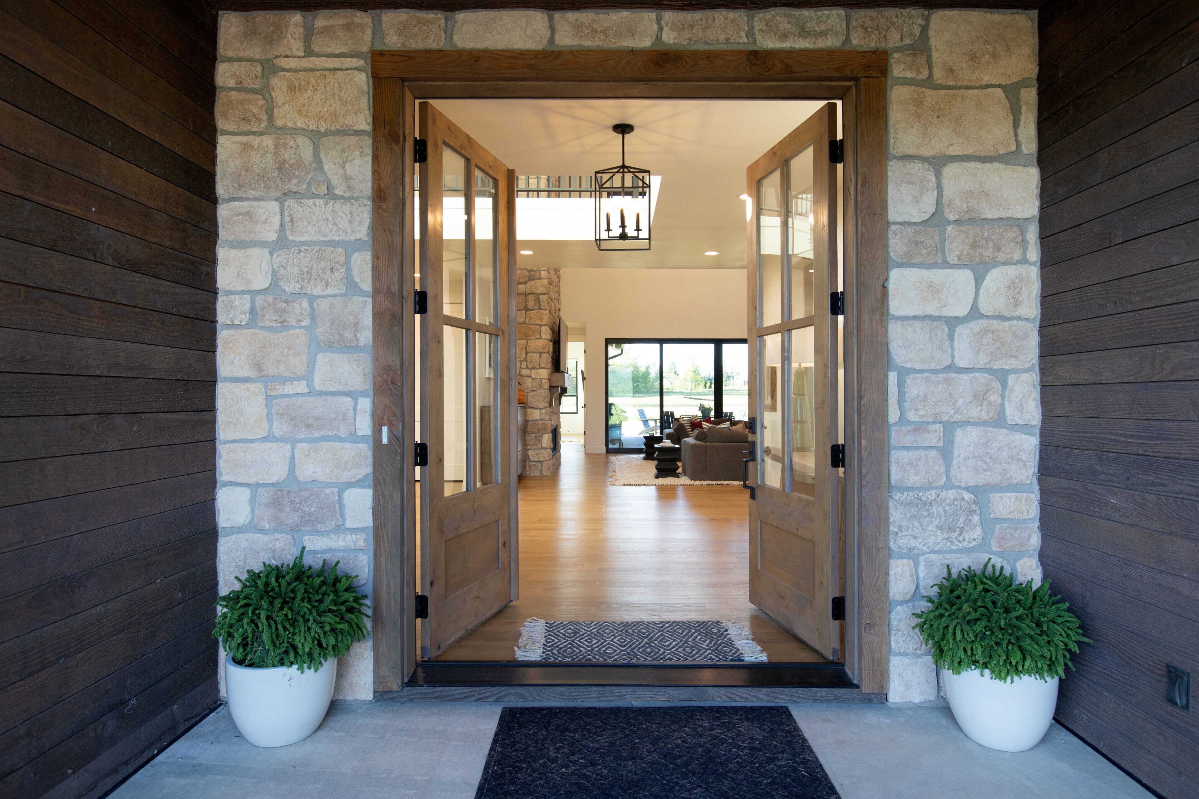 A stone entrance with a wooden door, a potted plant, and a view into a living area with a couch and a stone wall.